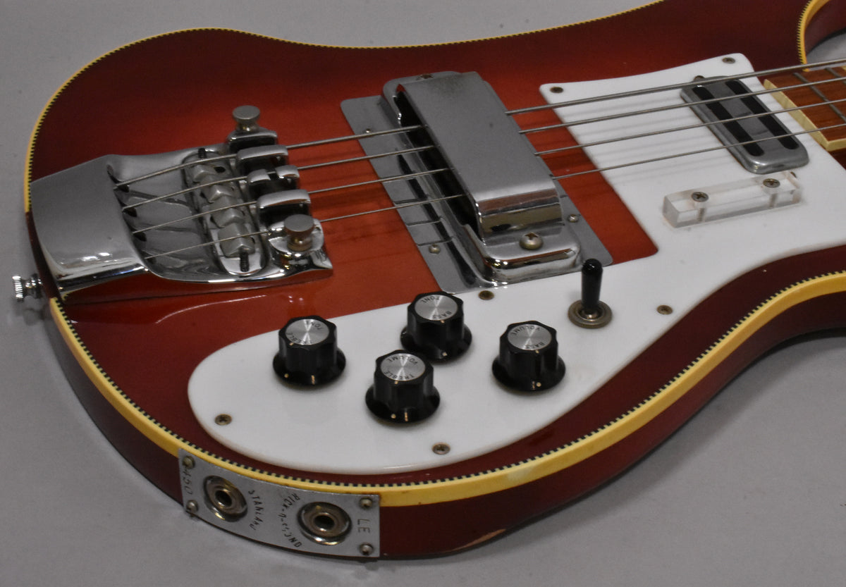 Close-up of the Fireglo bass body, showing the chrome bridge, pickup cover, white pickguard, four black knobs, and output jacks.