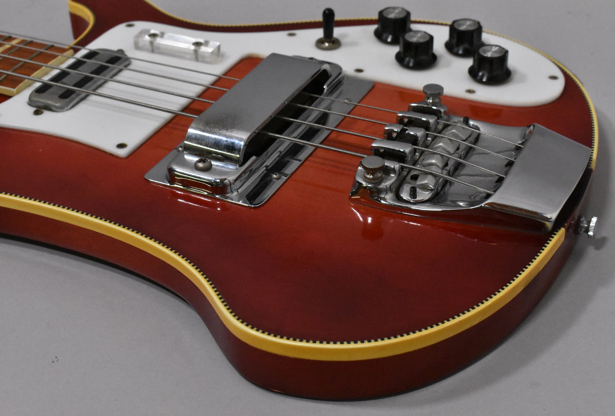 Close-up of the Fireglo bass body, showing the chrome bridge, pickup cover, white pickguard, and four black control knobs.