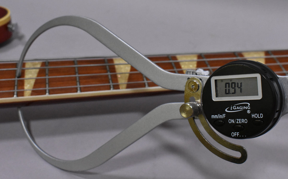 Digital calipers measure the bass's fretboard, showing a 0.94 reading, with triangular inlays visible on the dark wood.