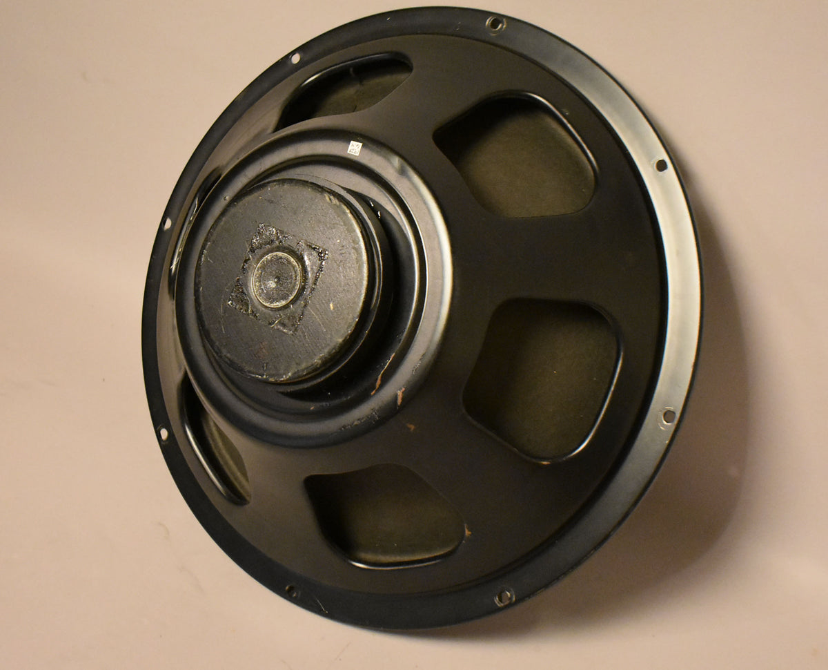 A dark gray speaker, viewed from an angle, shows its cone and magnet with visible wear and mounting holes around the rim.