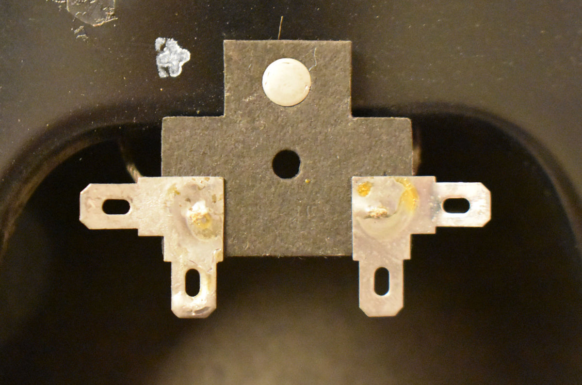 Close-up of the speaker's dark gray terminal board with a central mounting hole, flanked by two tarnished silver spade terminals.