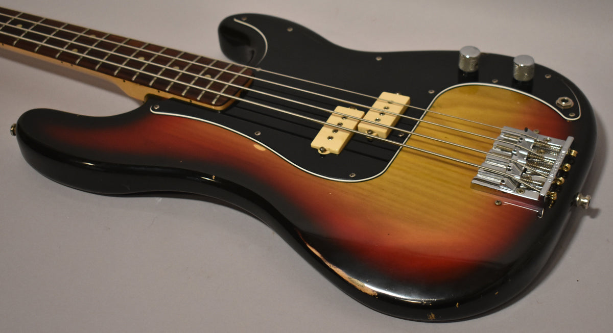 The bass body, angled from the neck, shows a sunburst finish with significant wear and chips on the lower bout, a black pickguard, and chrome hardware.