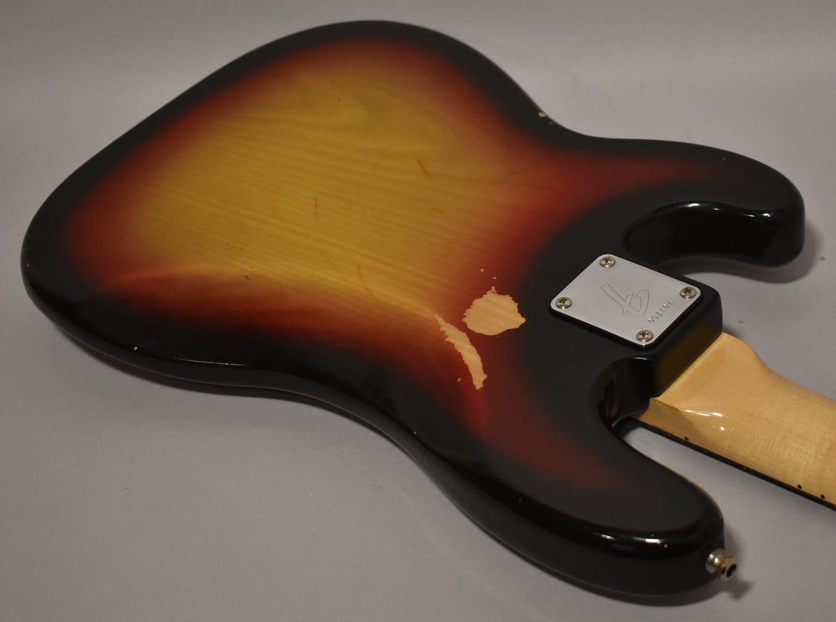 Rear view of a sunburst bass body with significant paint wear exposing wood, a chrome neck plate, and an output jack.