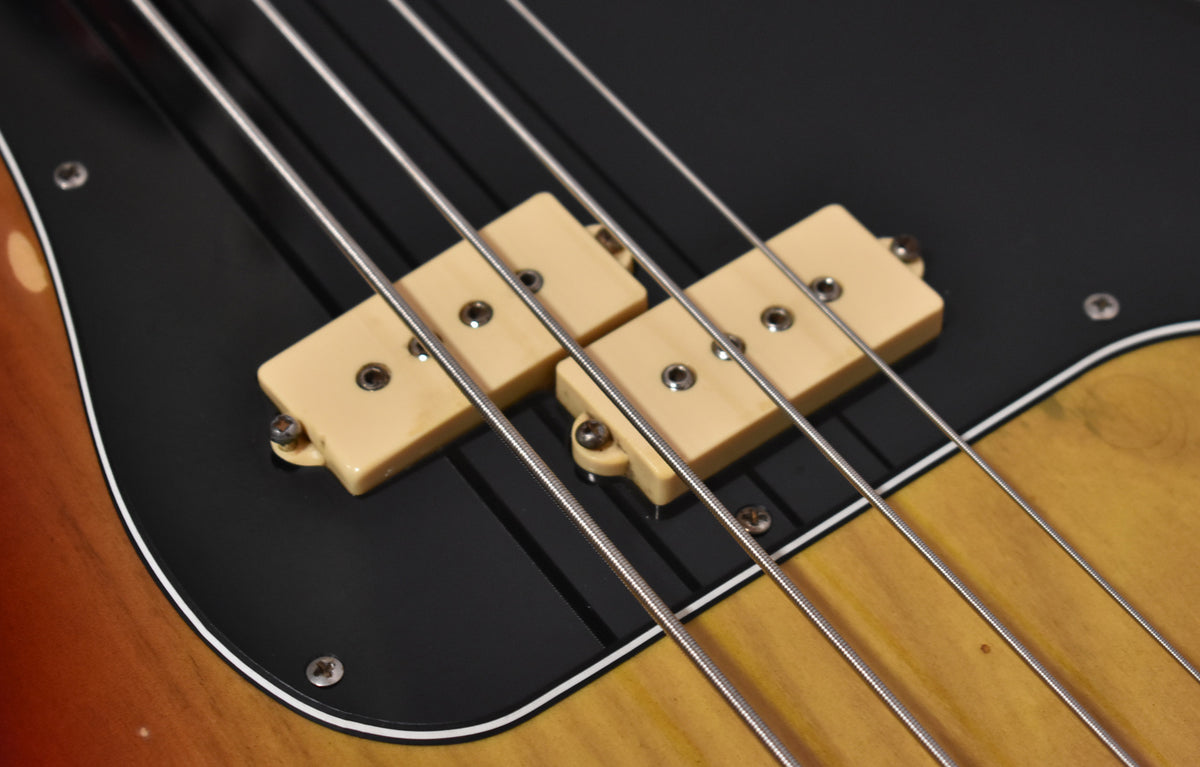 Close-up of the bass body, showing the black pickguard, cream split pickup, and sunburst finish with minor wear.