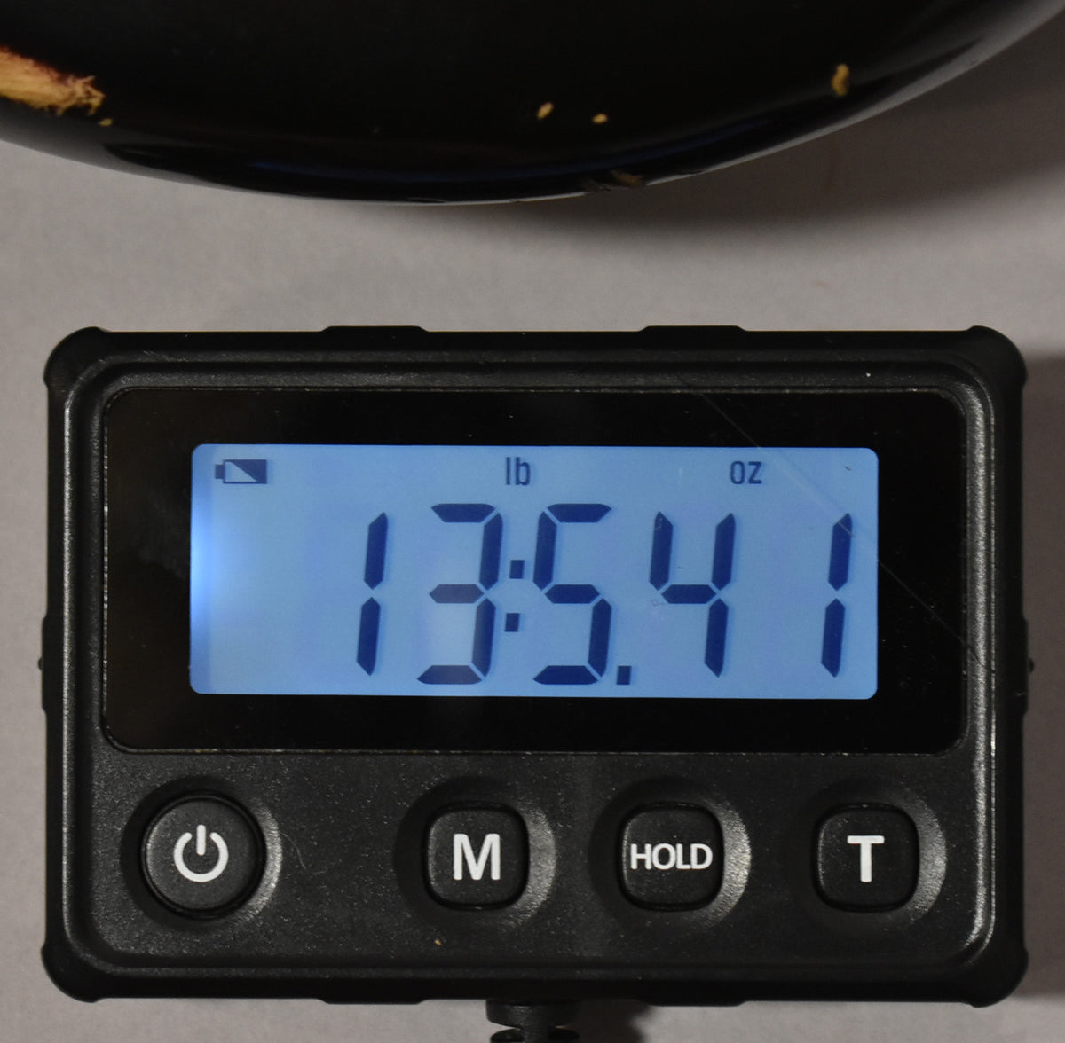 A digital scale displays "13:54 1" in lb and oz, with a dark object partially visible above it.