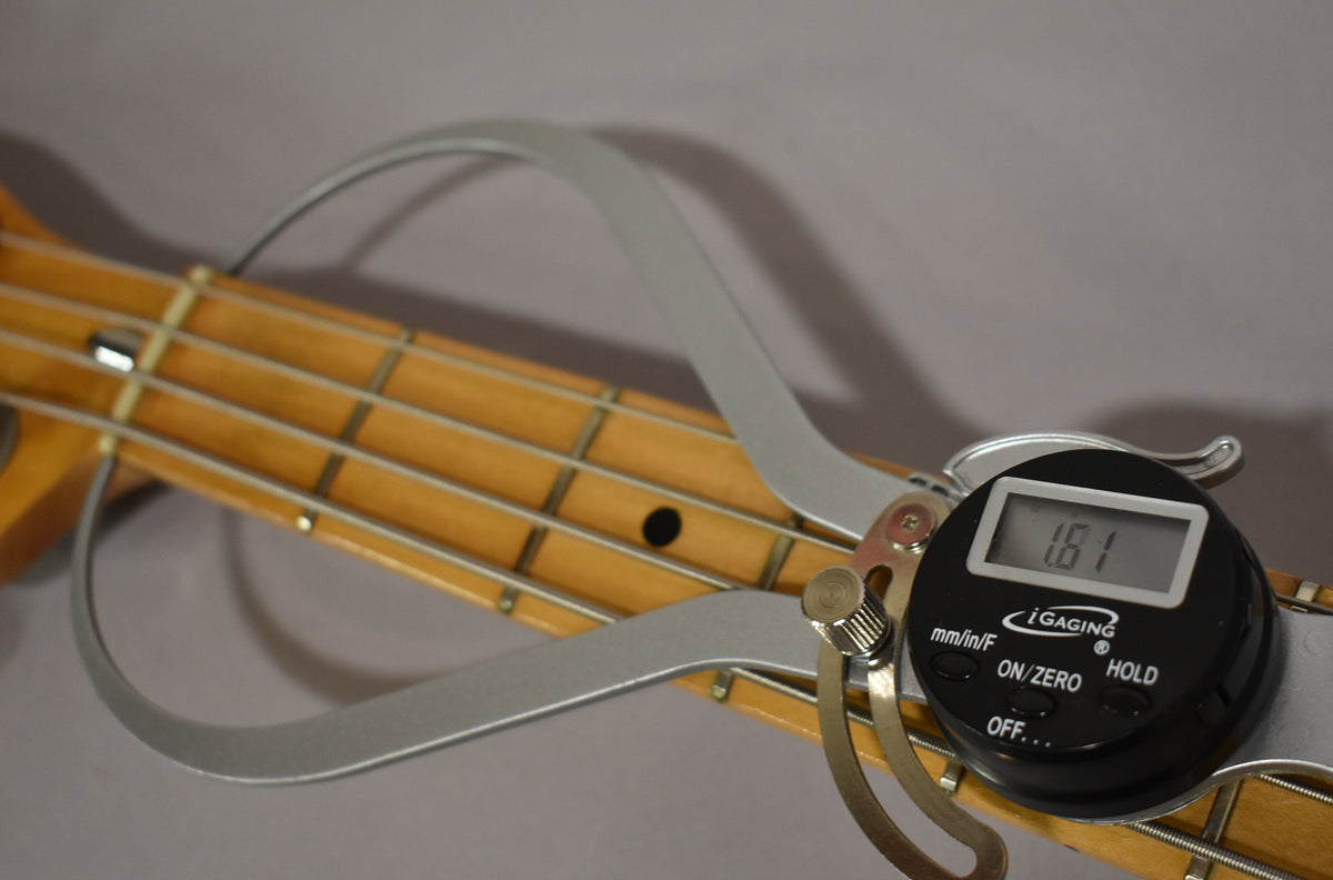 Close-up of the bass's maple fretboard with a digital caliper measuring fret height at 1.61mm, showing light wear on the frets.