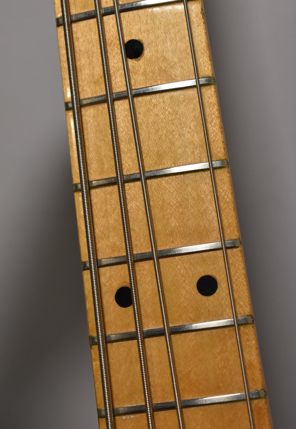 Close-up of the maple fretboard with black dot inlays and four strings, showing some wear on the frets.