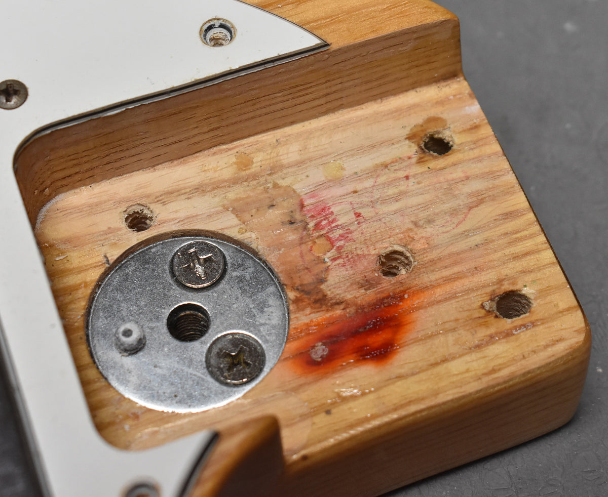 Close-up of the guitar neck pocket with exposed wood, screw holes, and red markings.