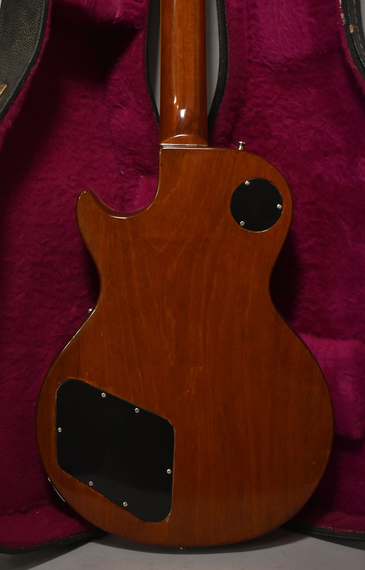 Full back view of the guitar, showing a glossy dark amber finish with light wear, two black control cavity covers, and a strap button.