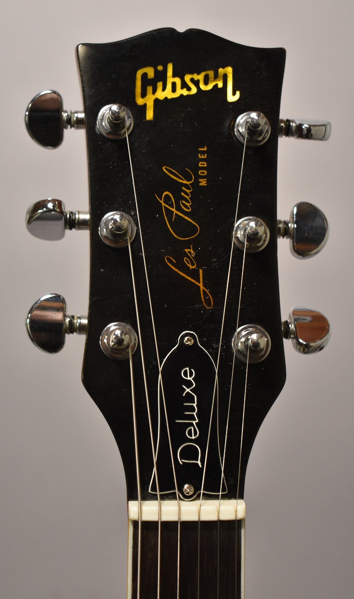 Close-up of the black headstock, showing six chrome tuners, a white nut, and the top of the dark fretboard.