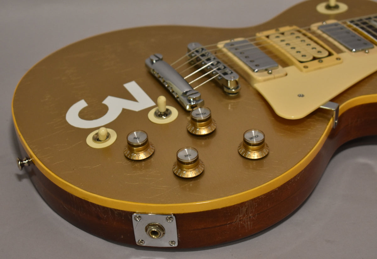 Close-up of the goldtop body with a large white "3", four gold "Volume" and "Tone" knobs, and heavy finish checking.