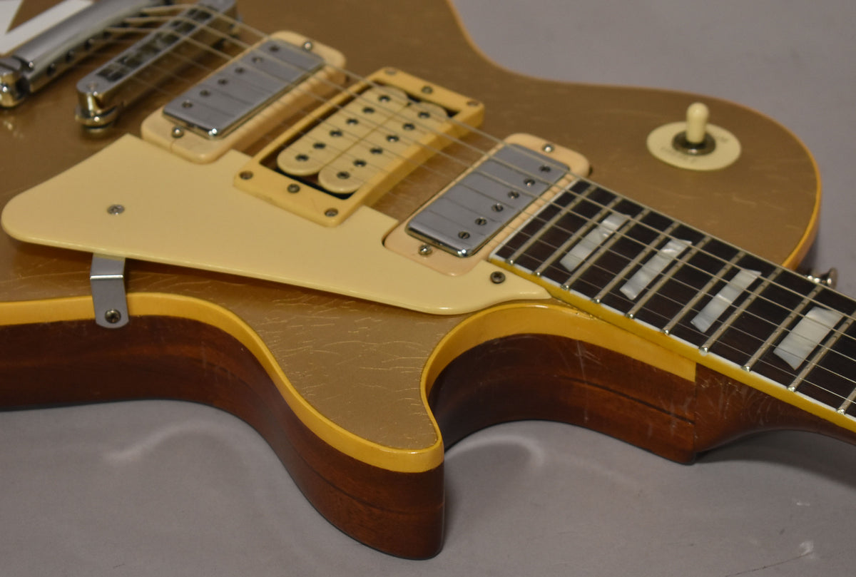 Close-up of a goldtop guitar body with a cream pickguard, two mini-humbuckers, and visible finish checking and wear.