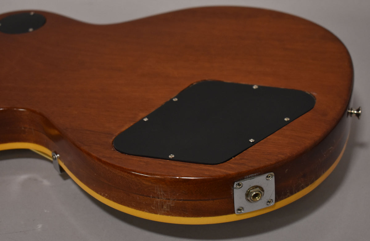 Angled view of the guitar's brown back, showing a black control cavity cover, output jack, and wear on the lower bout's binding.
