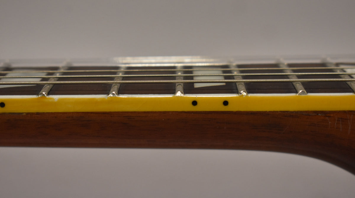 Close-up of the guitar's fretboard and neck, showing dark wood, yellowed binding with black side dots, and light fret wear.