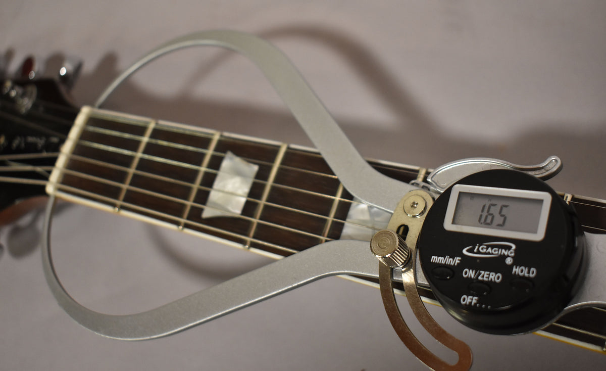 Close-up of the guitar's dark fretboard with trapezoid inlays, showing a digital caliper measuring the nut width at 1.65 inches.