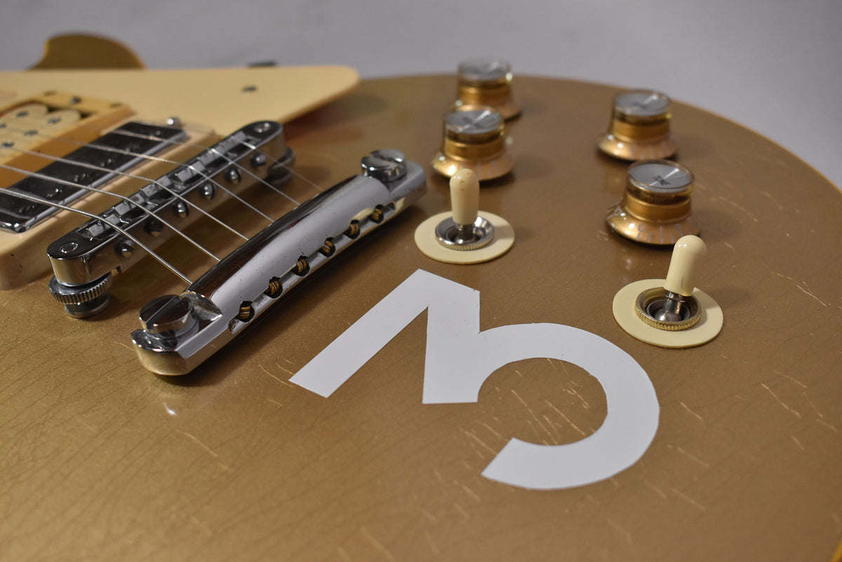 Close-up of the goldtop body, showing the bridge, tailpiece, four gold speed knobs, two cream toggle switches, and a large white "3" decal.