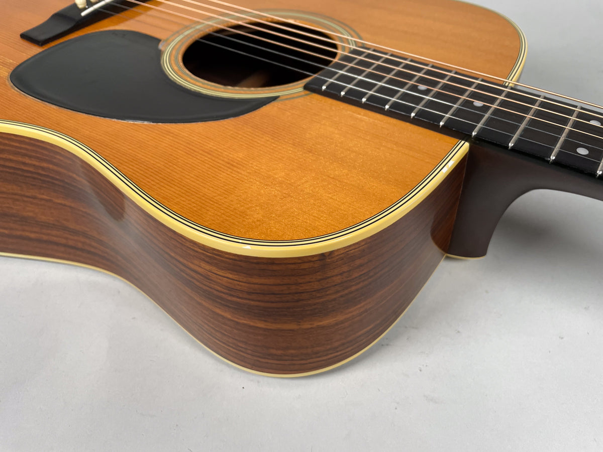 Close-up of the guitar's lower bout and waist, showing the light brown top, dark wood sides, black pickguard, and neck joint.
