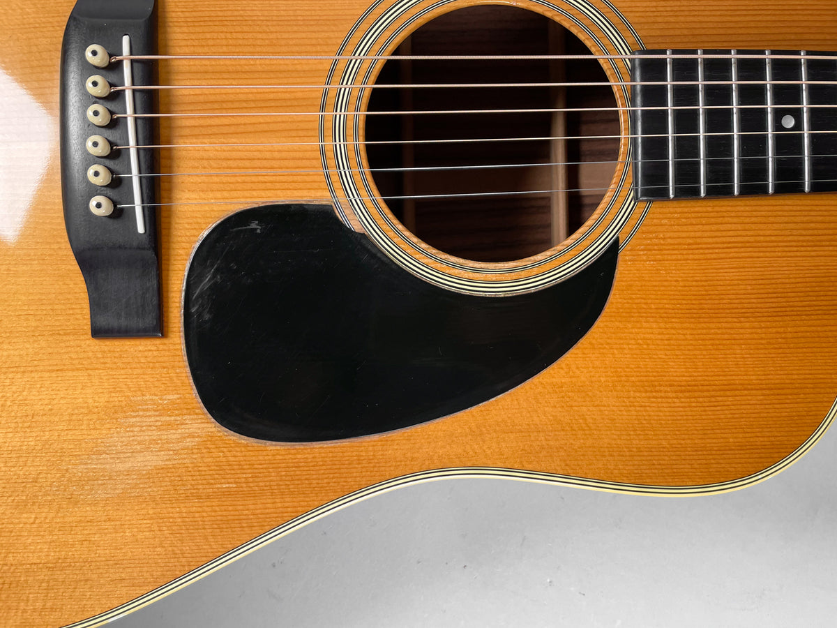 Close-up of the natural finish body, showing the soundhole, black pickguard with scratches, bridge, and lower fretboard.