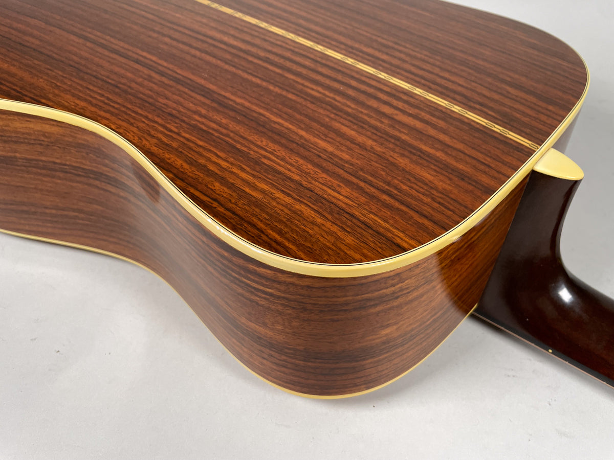 Close-up of the guitar's dark brown wood grain back and side, with a light binding and a visible neck heel.