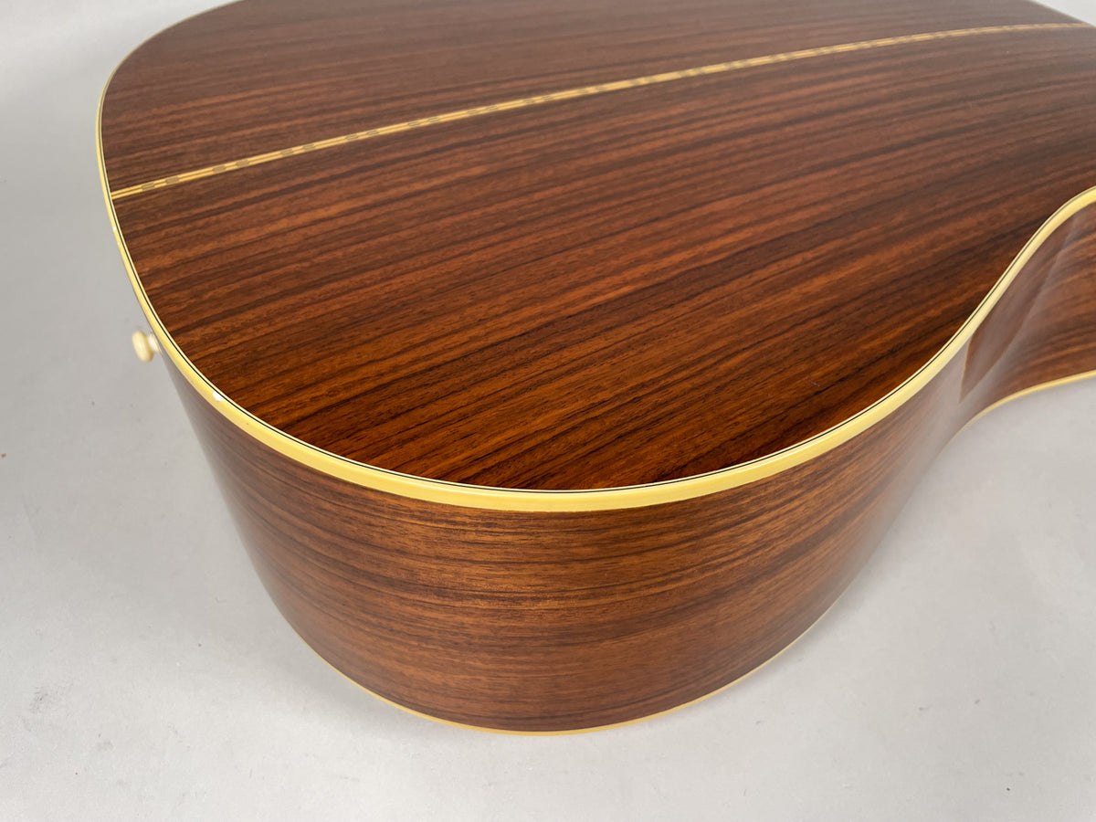The guitar's dark brown back and side are visible, with a light binding, and a thin light stripe down the center of the back.