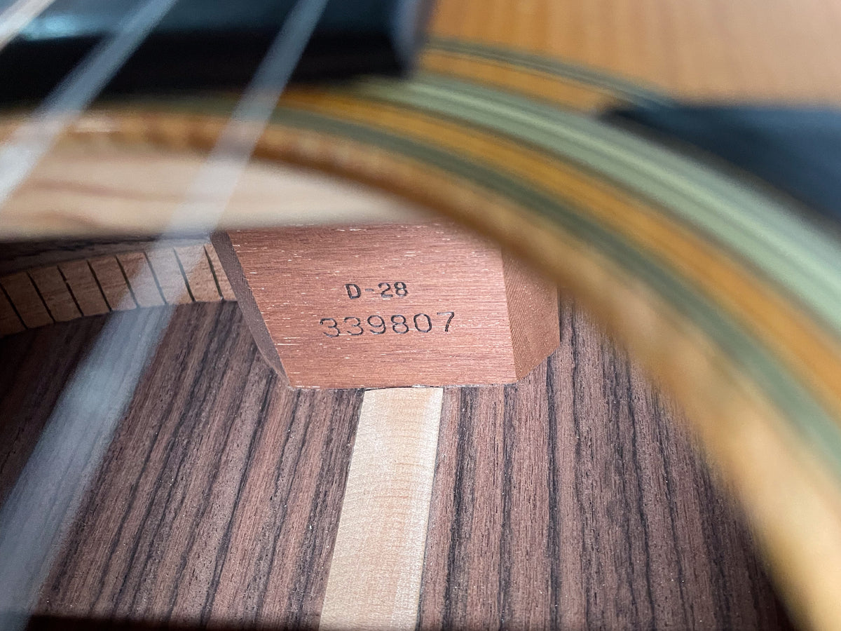 Close-up inside the soundhole shows the D-28 model and serial number 339807 stamped on the neck block, with wood grain visible.