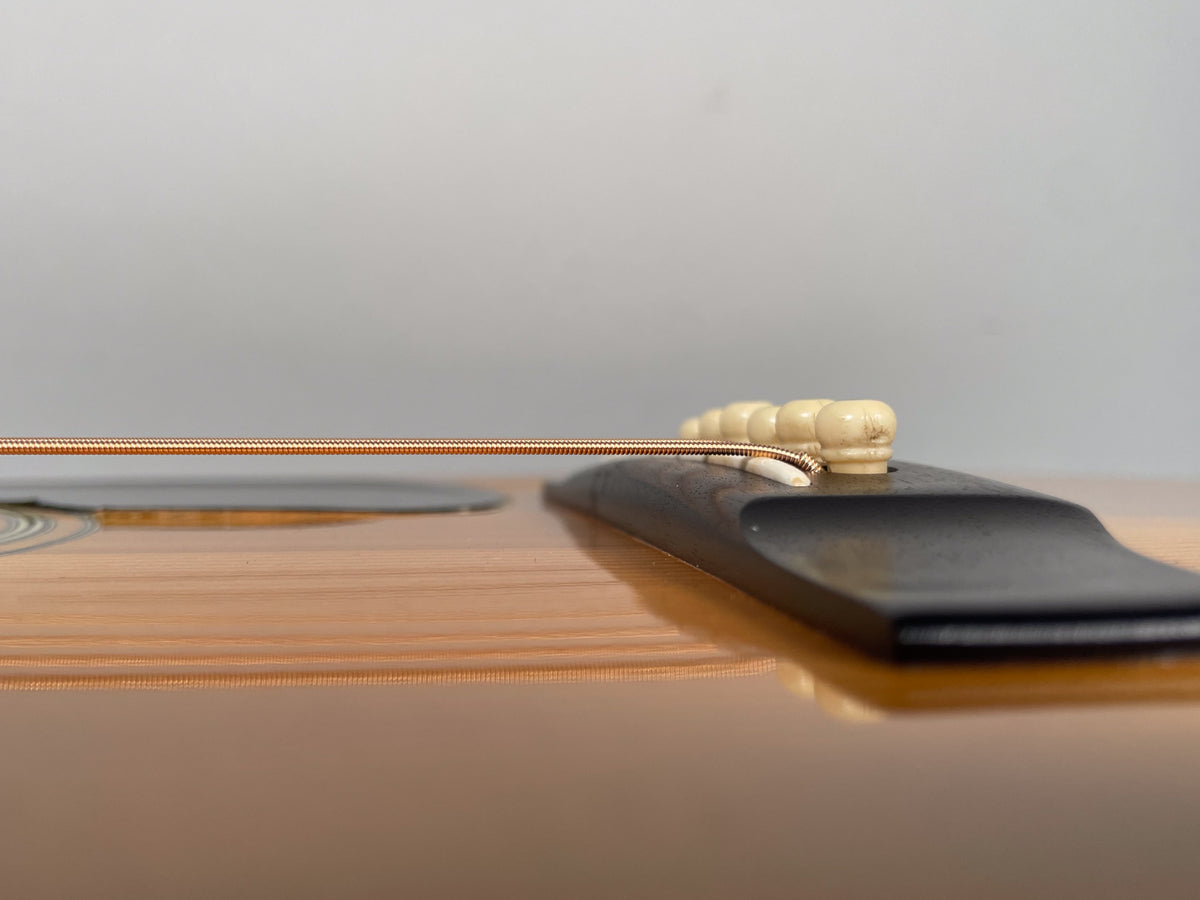 Close-up, low-angle view of the guitar's light-colored spruce top, dark bridge, and six cream-colored bridge pins with visible wear.