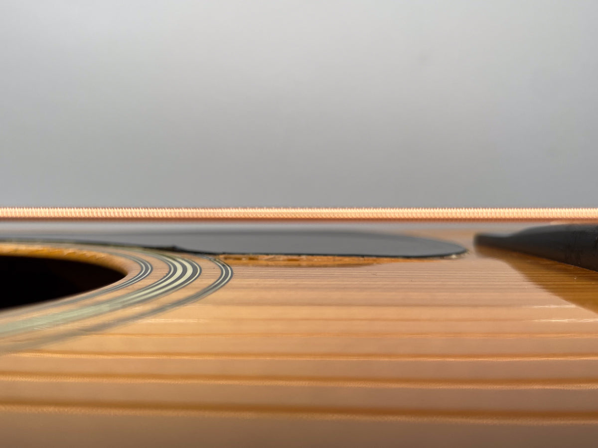 Extreme close-up of the guitar's light-colored spruce top, showing the soundhole rosette and pickguard, with visible finish checking.