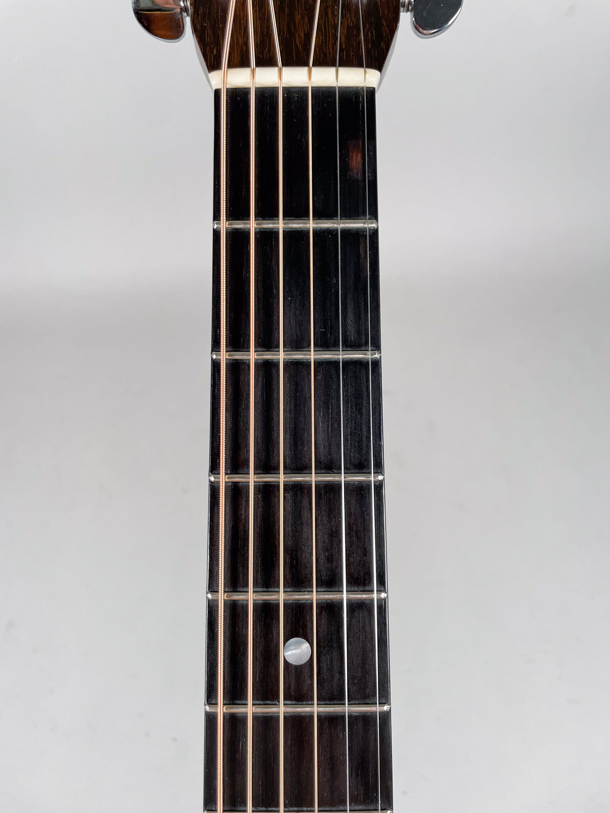 Close-up of the dark, worn fretboard and strings, showing a single round mother-of-pearl inlay at the 7th fret.