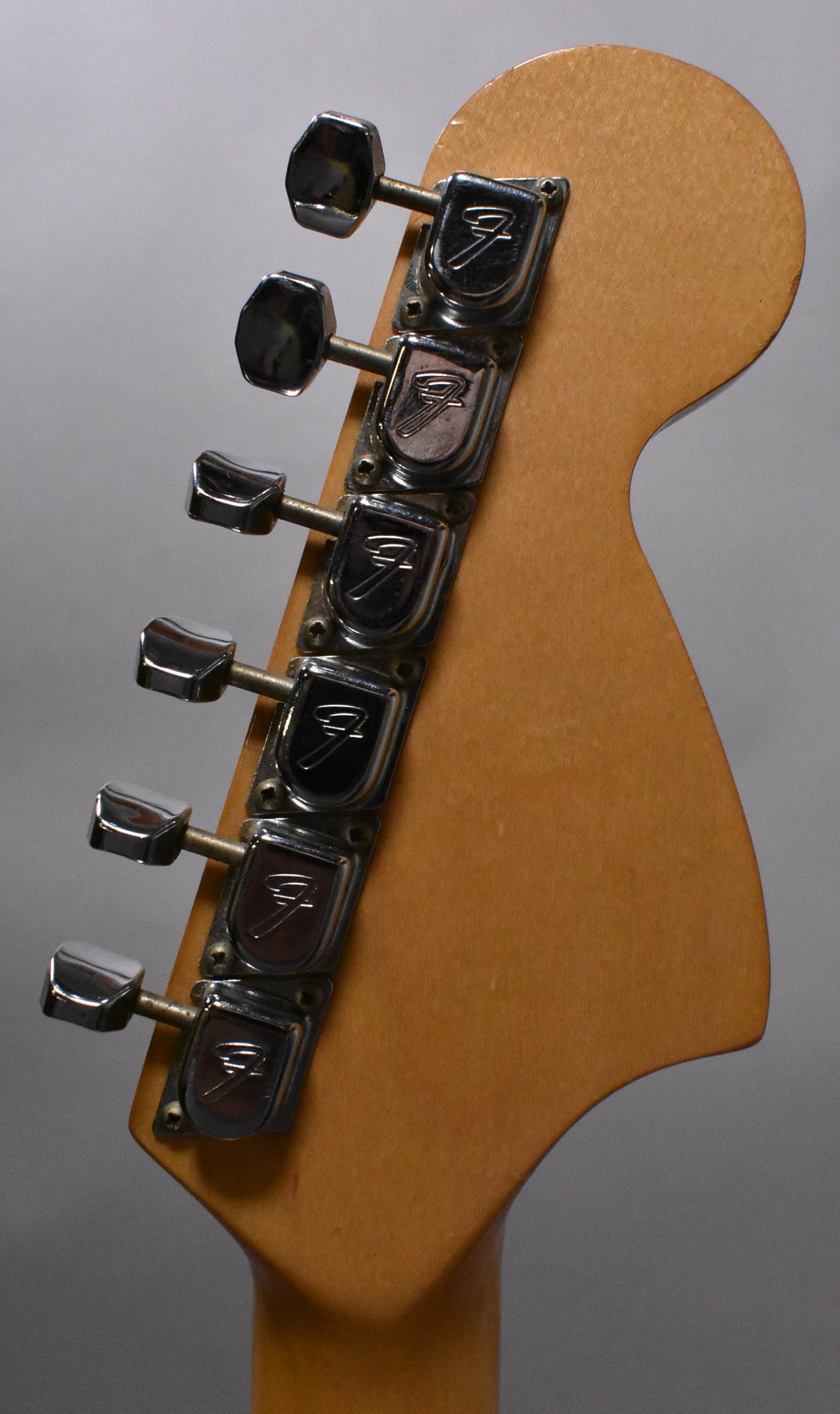The back of a light brown headstock with six chrome tuners, showing some wear and tarnishing on the metal.
