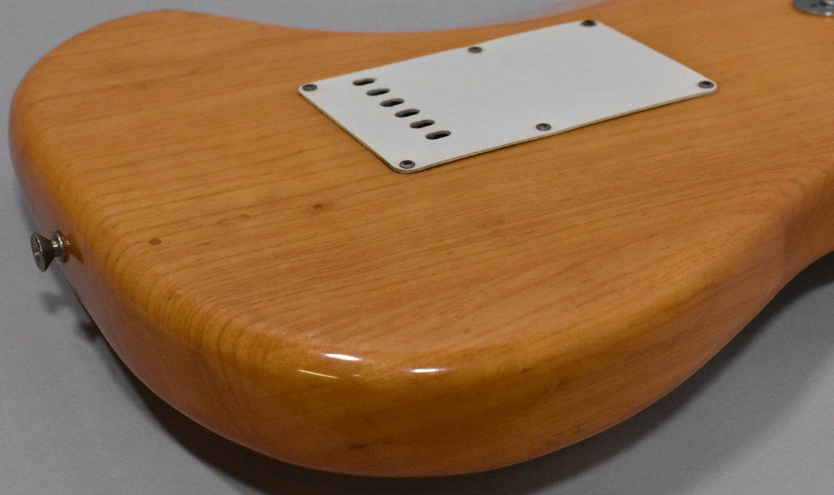 The back of the natural ash body shows a white tremolo cover, strap button, and visible wood grain with minor surface imperfections.