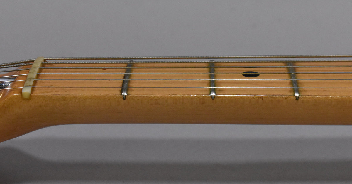 Close-up of the maple fretboard and neck, showing the nut, frets, strings, and a dark circular inlay at the 7th fret.