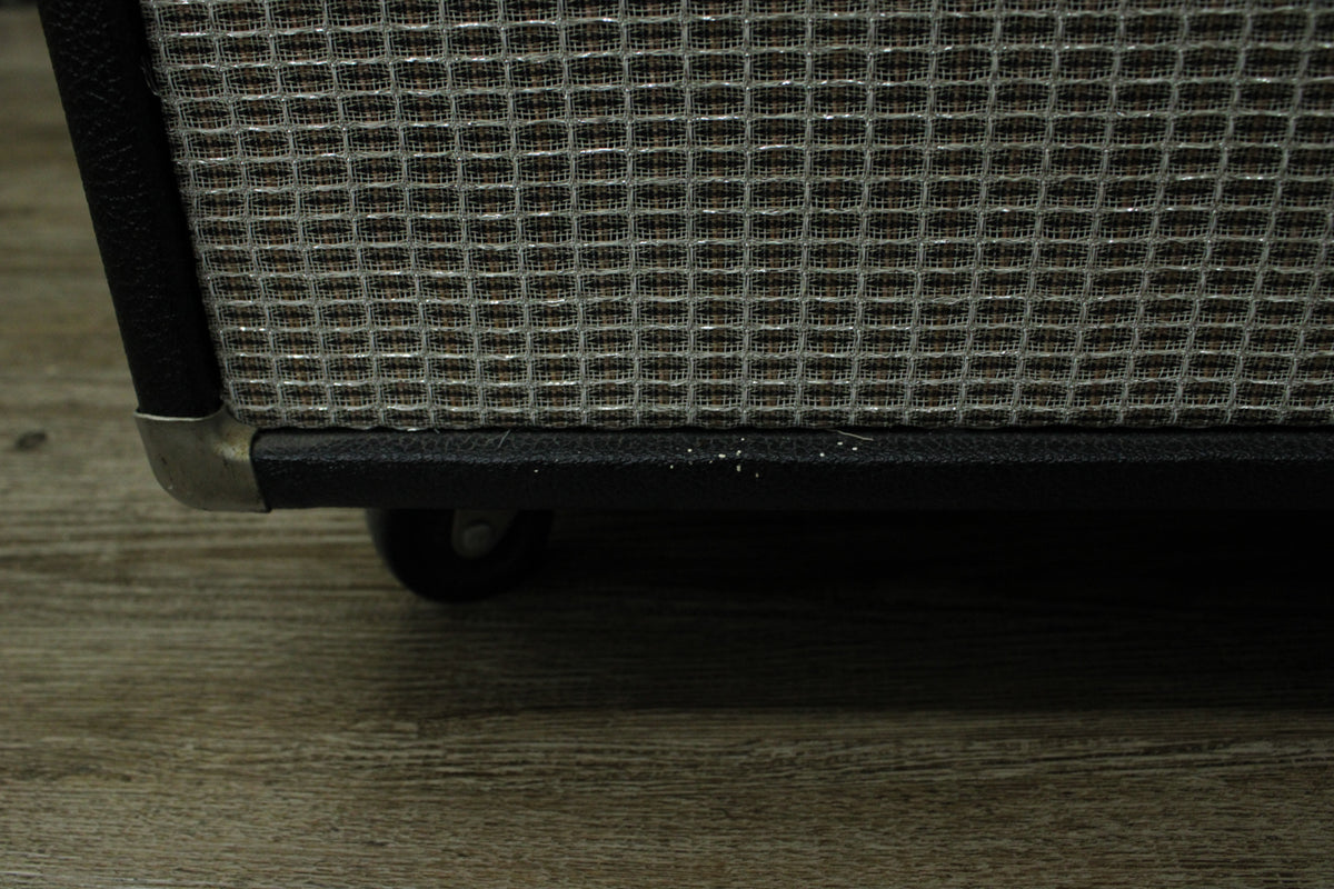Close-up of the amp's bottom right corner, showing the silver grille cloth, black tolex, metal corner protector, and a caster wheel.