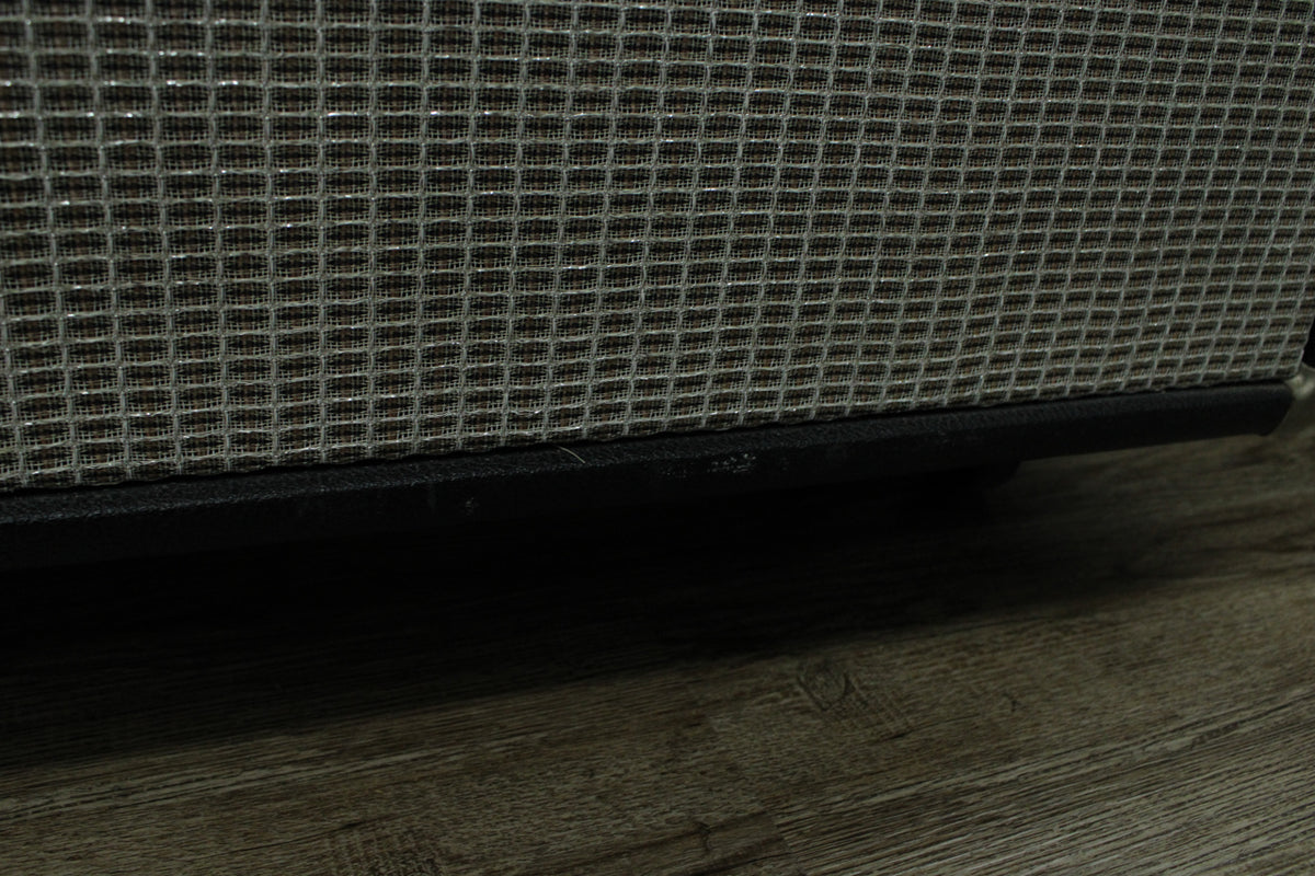 Close-up of the amp's bottom edge, showing the silver grille cloth, black trim, and minor scuffs on the wood floor.