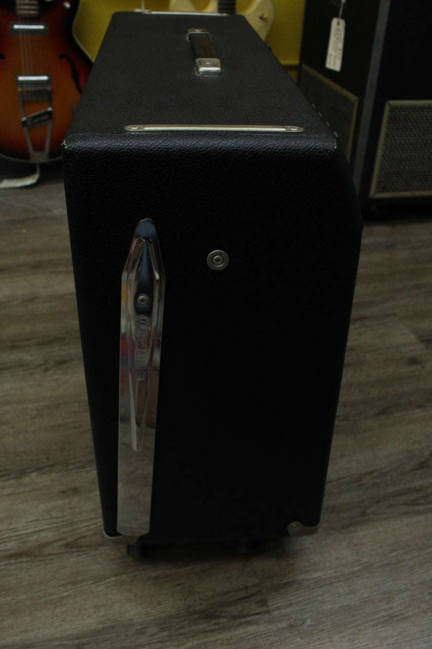 Angled view of the black textured amp cabinet, showing the chrome side handle, top handle, and metal corner protectors.
