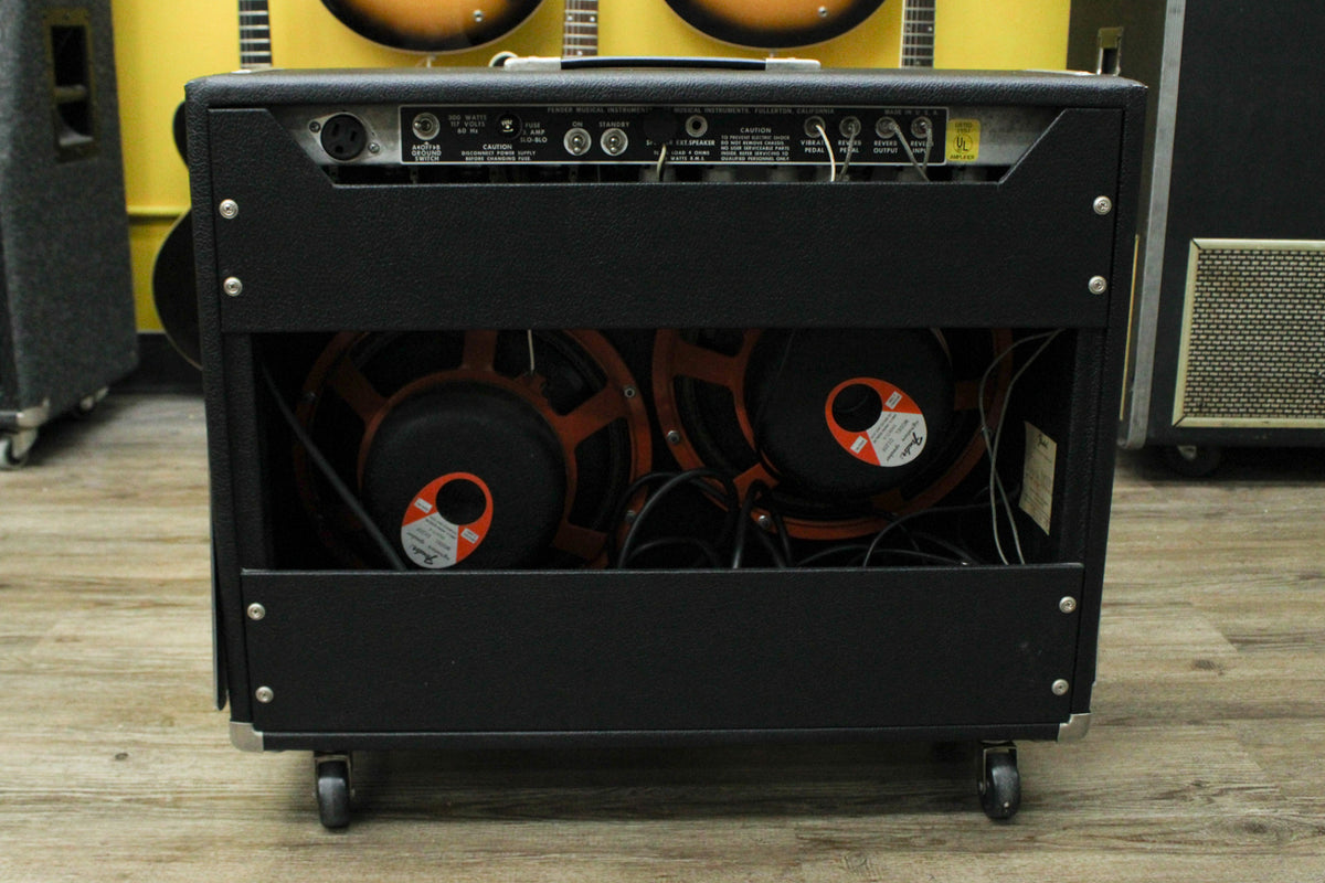 Rear view of a black guitar amp with two orange-framed speakers visible, showing the silver control panel with various inputs and outputs.