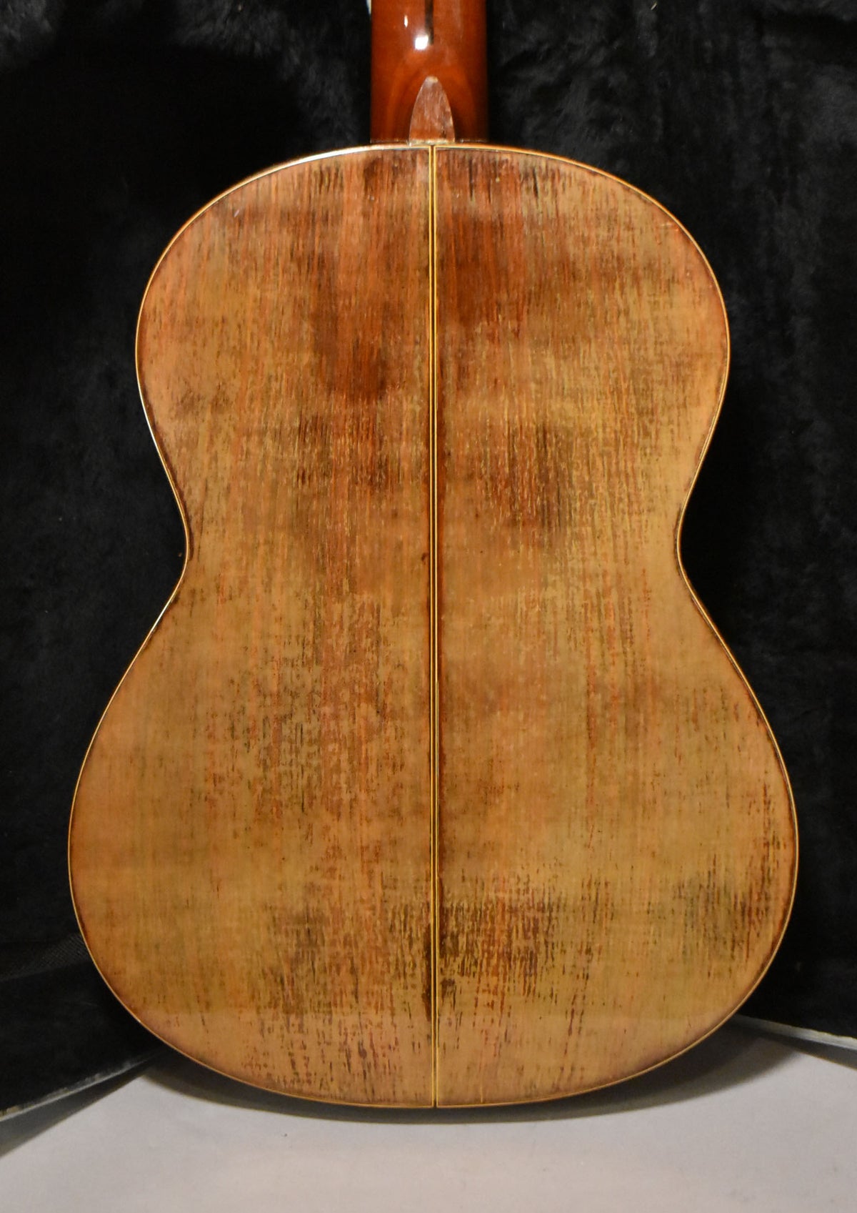 Full back view of a classical guitar with a worn, reddish-brown finish, showing a center seam and light binding.