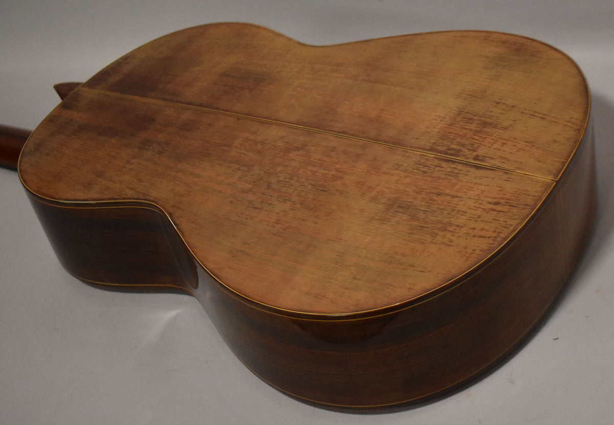 The classical guitar's back and sides are shown from above, revealing a worn, matte light brown back and glossy dark brown sides.