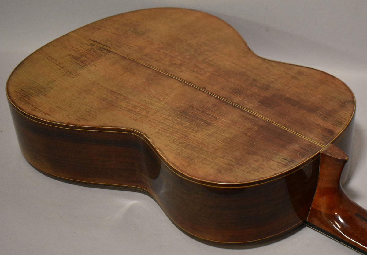 The guitar's back and sides are visible, showing a worn, light brown back with a center seam and dark brown, glossy sides.