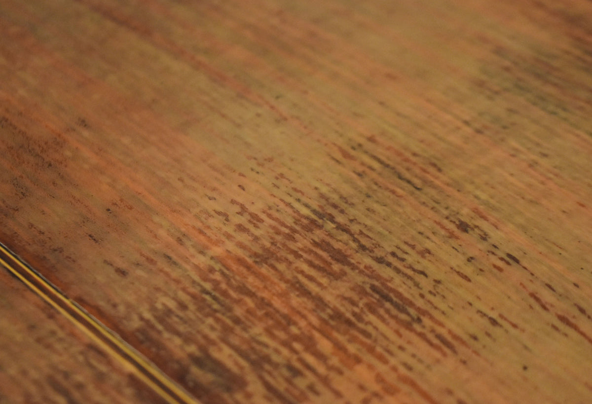 Close-up of the guitar's worn, light brown wooden top, showing dark streaks and a thin, light-colored binding on the lower left.