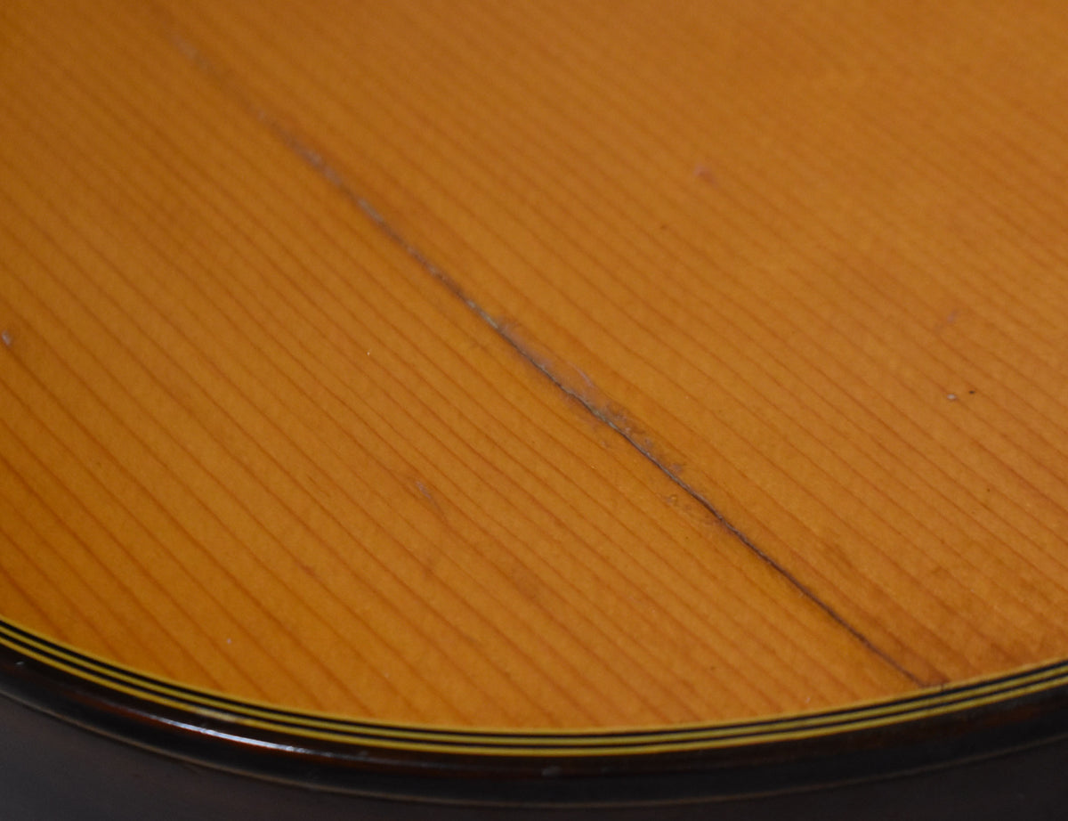 Close-up of the guitar's light brown top, showing a long, dark crack running diagonally across the grain and a dark binding.