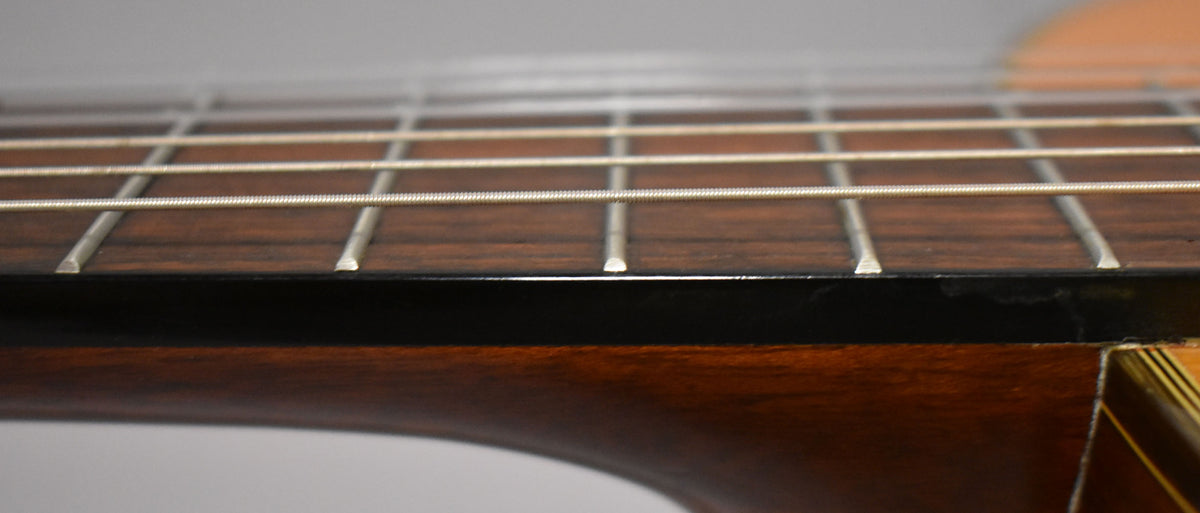 Close-up of the classical guitar's dark brown fretboard and frets, with light strings running across it and some finish wear visible.