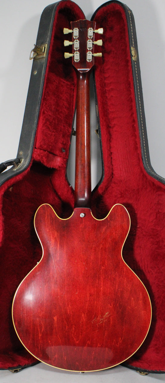 Full rear view of a cherry semi-hollow guitar with a dark neck, six cream tuners, and a few scratches on the body.