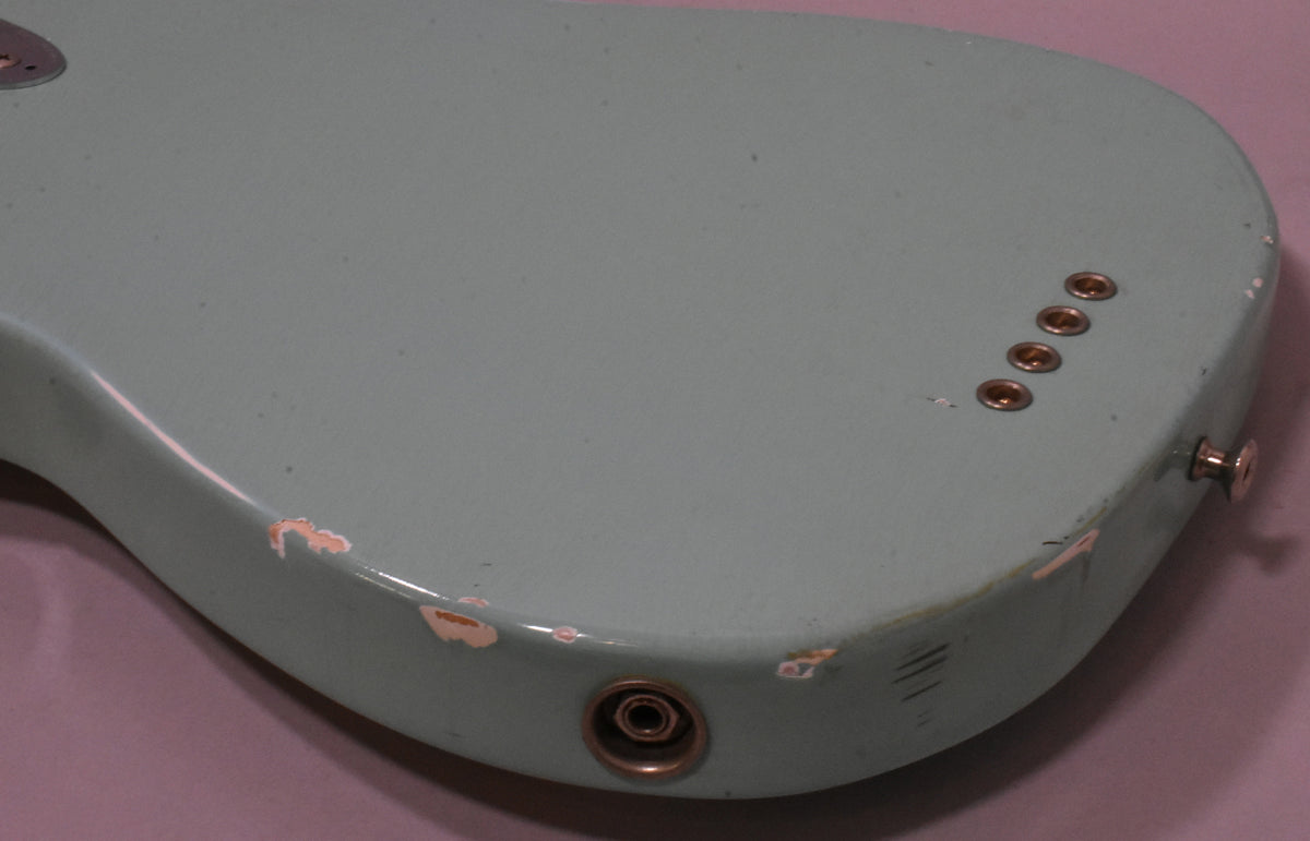 Close-up of the bass body's bottom edge, showing the light blue finish with significant chipping, four string ferrules, and output jack.