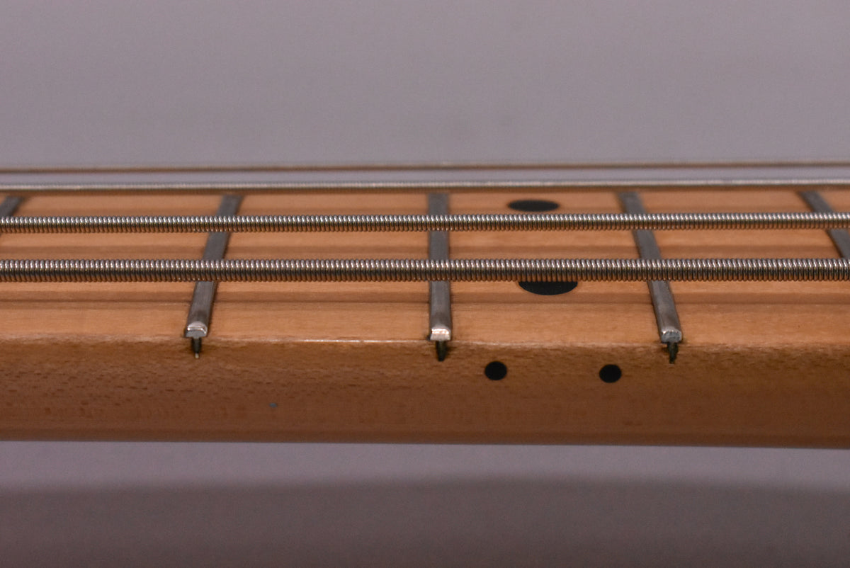 Close-up of the maple fretboard and frets, showing black dot inlays and some wear on the fret edges.