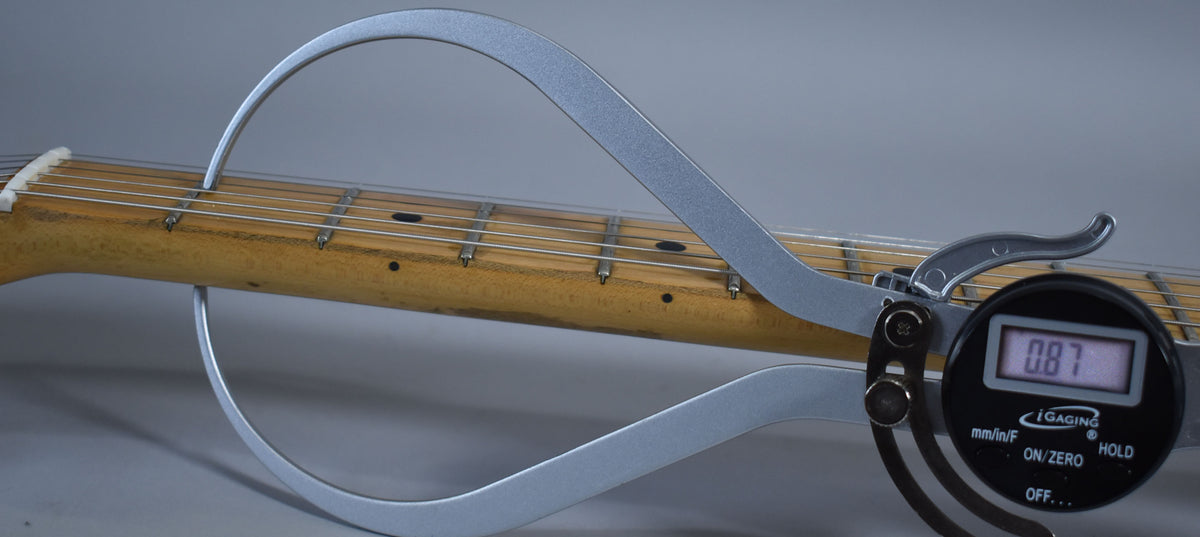 A digital caliper measures the neck thickness of the natural finish maple neck, displaying "0.87" on its screen.