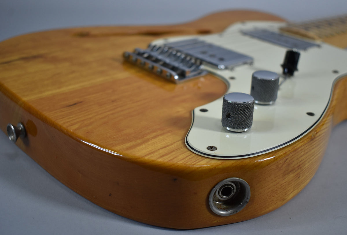 Close-up of the natural finish body, showing the output jack, two knurled chrome knobs, and a white pickguard with some wear.