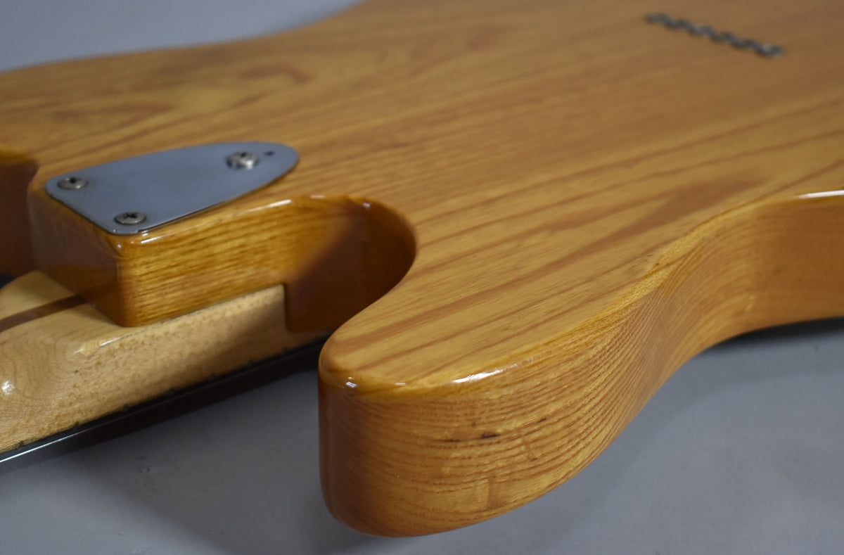 Close-up of the guitar's lower body in natural wood finish, showing the neck plate, string-through ferrules, and minor dings.