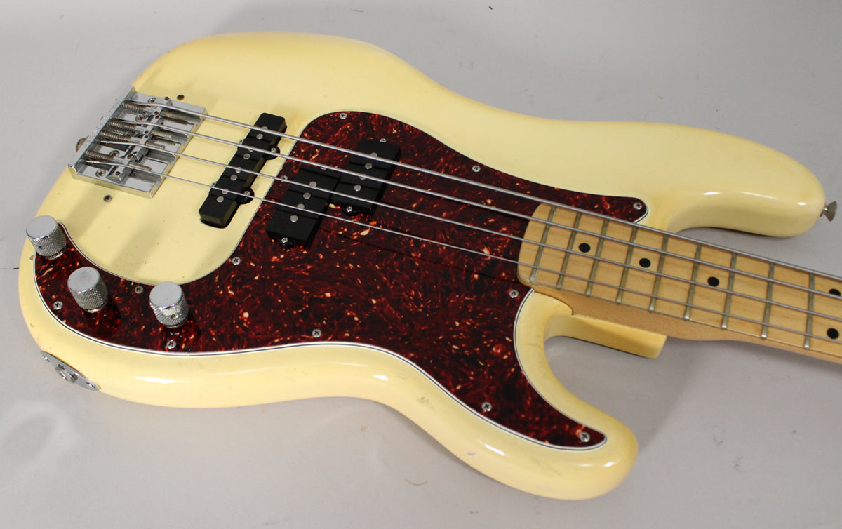 The bass body is angled from the upper left, showing its creamy white finish, tortoiseshell pickguard, chrome bridge, and three knurled knobs.