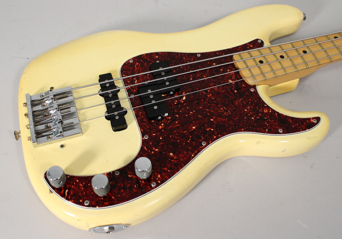 The off-white bass body, with a tortoiseshell pickguard and chrome hardware, shows visible wear and checking on its finish.
