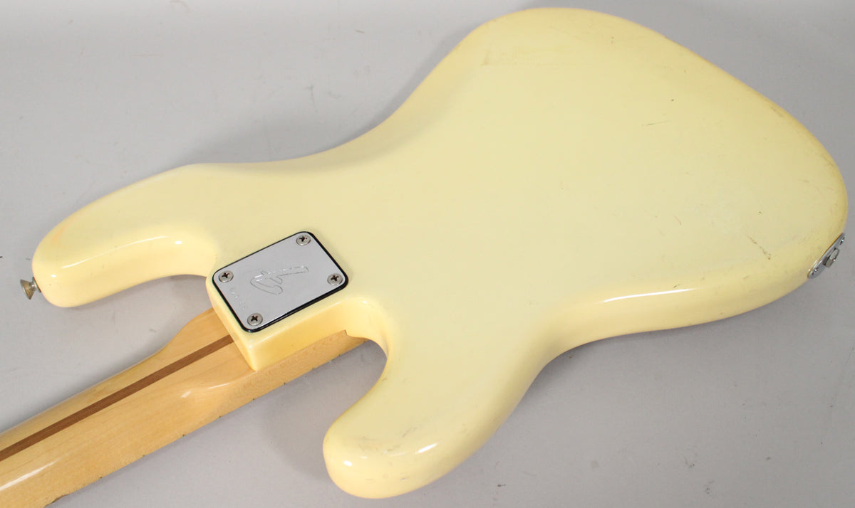 The back of an Olympic White bass body with a chrome neck plate, showing finish wear and a light-colored maple neck.